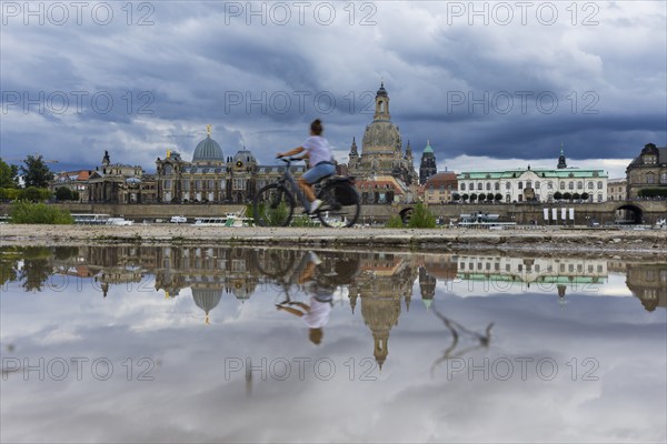 The Dresden silhouette with a cyclist and dark clouds behind the Church of Our Lady is reflected in