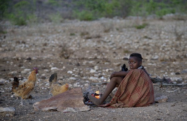 Young shepherdess from the Himba people sitting by a campfire, Ombombo, Kaokoland, Kunene, Namibia,