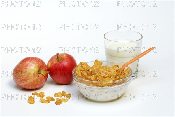 Glass bowl with cornflakes, apples, glass with milk, spoon, bowl