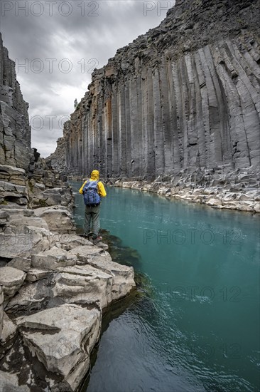 Tourist standing by the river in Stuðlagil Canyon, turquoise blue river between basalt columns,