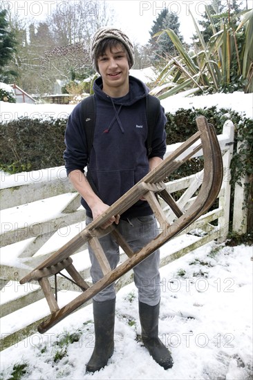 Model released portrait of teenage boy in the snow holding a wooden sledge, Suffolk, England,