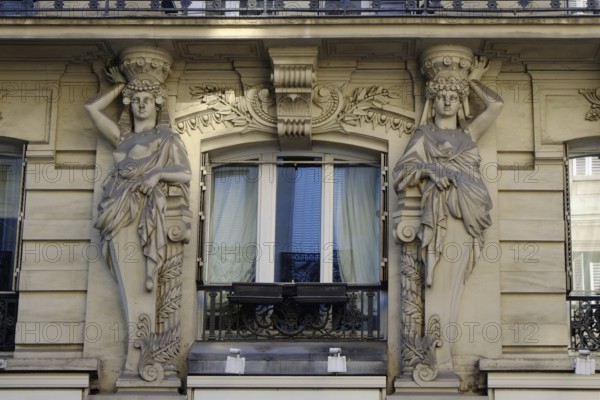 Two stone caryatids frame a window in the façade of a house in Paris as a decorative element.