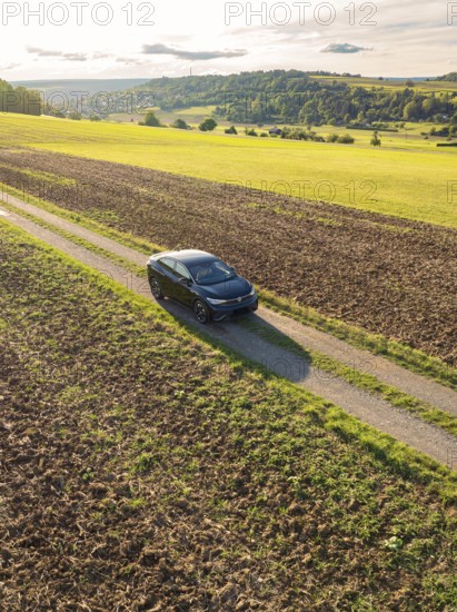 A car drives on a dirt track between large fields under a sky with clouds and evening sun, car