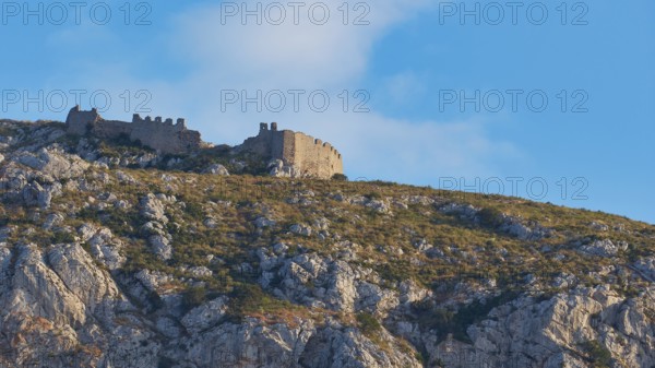 An ancient castle on the top of a rocky mountain under a blue sky with clouds, Archaic Castle,