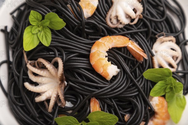 Black cuttlefish ink pasta with shrimps or prawns and small octopuses on gray wooden background and