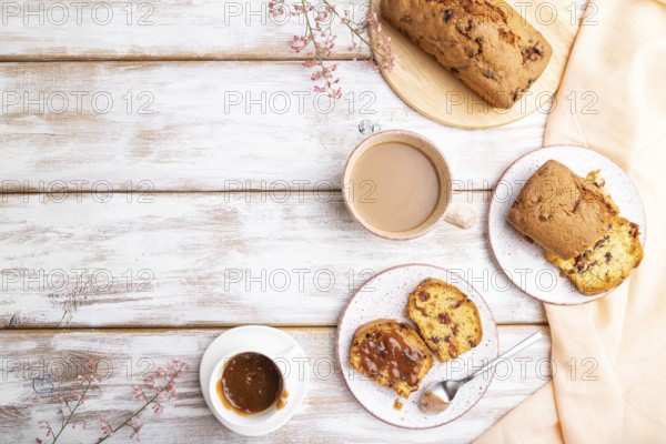 Homemade cake with raisins, almonds, soft caramel and a cup of coffee on a white wooden background