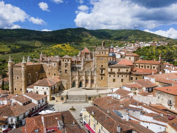 Aerial view of an old monastery with red roofs and surrounding hills under a blue sky in Spain. The