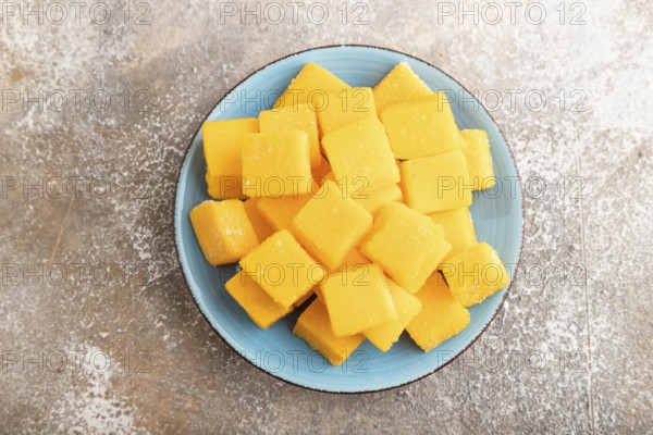 Dried and candied mango cubes on blue plate on brown concrete background. Top view, flat lay, close