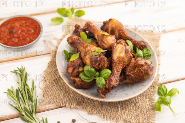 Smoked chicken legs with herbs and spices on a ceramic plate with linen textile on a white wooden