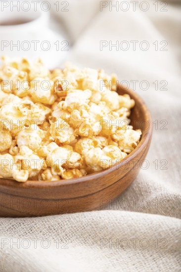 Popcorn with caramel in wooden bowl and a cup of coffee on a white wooden background and linen