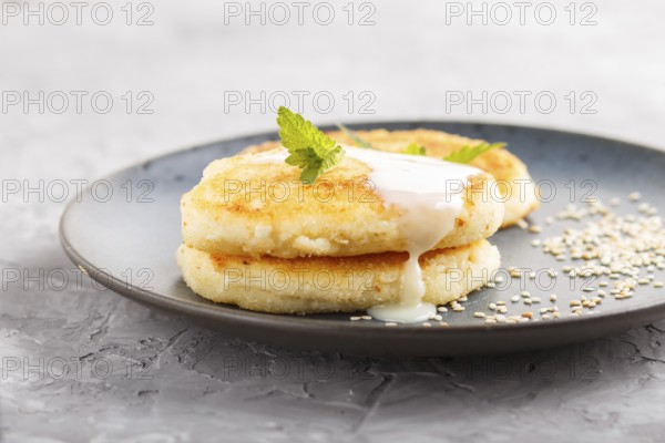 Cheese pancakes on a blue ceramic plate with milk sauce on a gray concrete background. side view,
