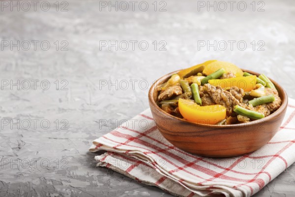 Fried pork with peaches, cashew and green beans in a wooden bowl on a gray concrete background.