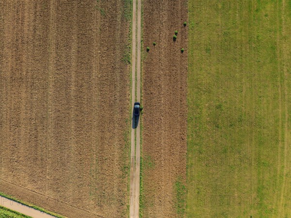 Aerial view of a car on a rural road between fields painted in green and brown colours, car