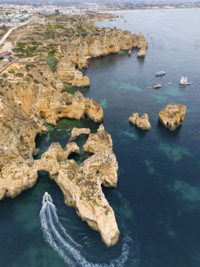 Rocks and cliffs rising out of the blue sea with a boat in the foreground, aerial view, Ponta da