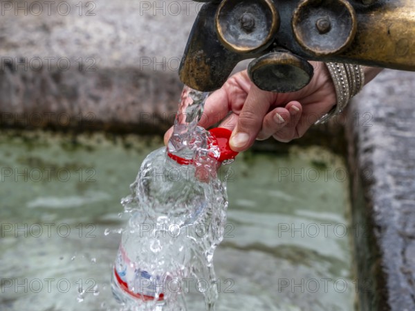 Water fountain, a woman fills drinking water into a small plastic bottle, Munich, Bavaria, Germany,