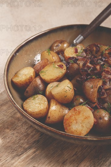 A bowl of perfectly roasted potatoes is served with caramelized onions and sprinkled with fresh