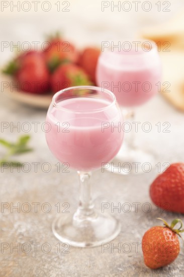 Sweet strawberry liqueur in glass on a gray concrete background and orange textile. side view,