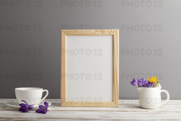 Beige wooden frame mockup with snowdrop crocus flowers and white coffee cup on gray paper