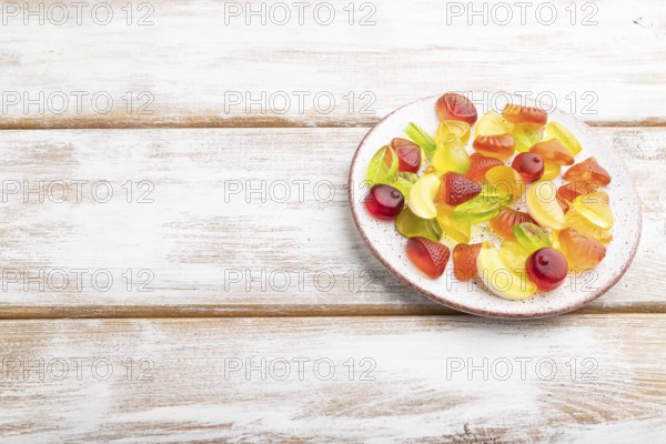Various fruit jelly candies on plate on white wooden background. side view, copy space