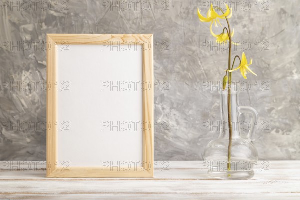Wooden frame with yellow trout lily or dogtooth violet flowers in glass on gray concrete background