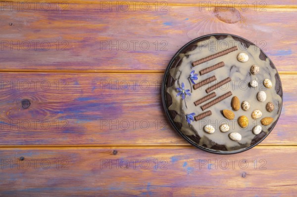 Homemade chocolate brownie cake with caramel cream and almonds on a colored wooden background. top