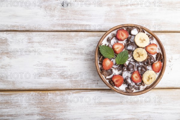 Chocolate cornflakes with milk and strawberry in wooden bowl on white wooden background. Top view,