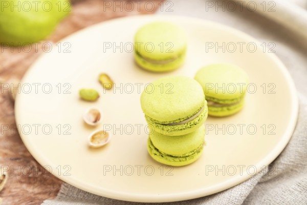 Green macarons or macaroons cakes with cup of coffee on a brown concrete background and linen