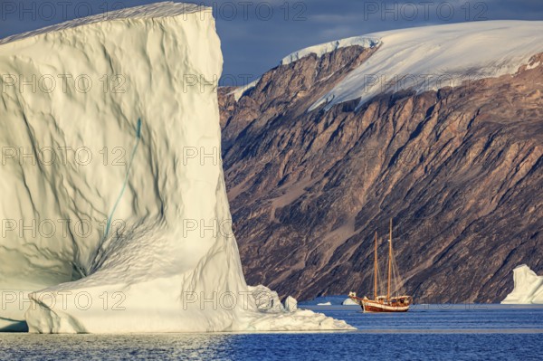 Sailing boat, ship in fjord in front of large icebergs and mountains, evening light, Scoresby