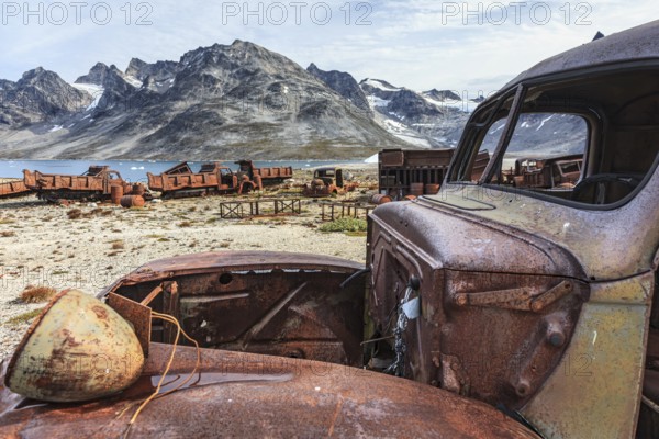 Rusted car and oil drums in front of steep mountains, remains of a US airbase from the Second World