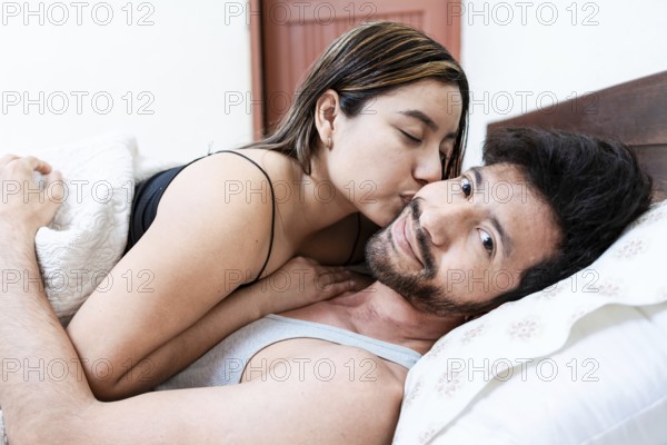 Woman kissing her husband on the forehead in bed, Wife in bed kissing husband on the forehead