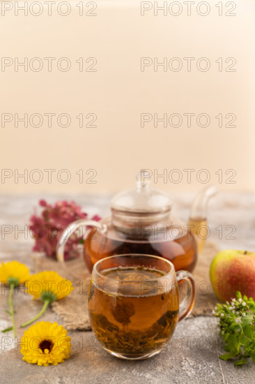 Red tea with herbs in glass teapot on brown concrete background and linen textile. Healthy drink