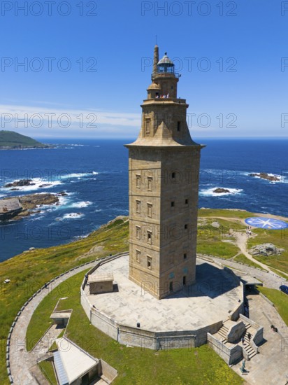 High lighthouse on the coast, rising proudly above the blue sea and the surrounding green areas,