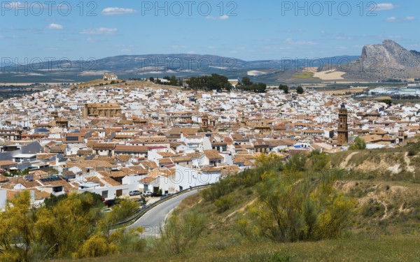 Spanish town with white buildings on a hill against a mountain backdrop under a blue sky,