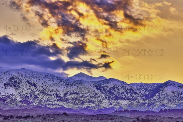 Dramatic sunset over snowy mountains with purple and orange sky and clouds, Lefka Ori, White