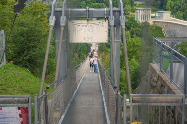 People crossing a metal suspension bridge over a green gorge, Rappbodetalsperre, Harz Mountains,