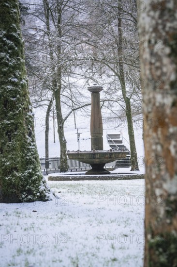 A snow-covered fountain surrounded by peaceful trees in winter, spa garden, Bad Wildbad, Black