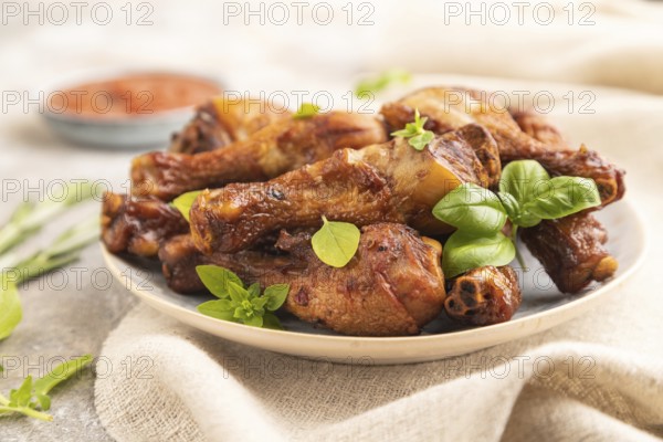 Smoked chicken legs with herbs and spices on a ceramic plate with linen textile on a brown concrete