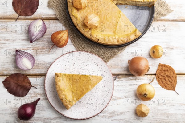 Autumn onion pie decorated with leaves and cup of coffee on white wooden background and linen