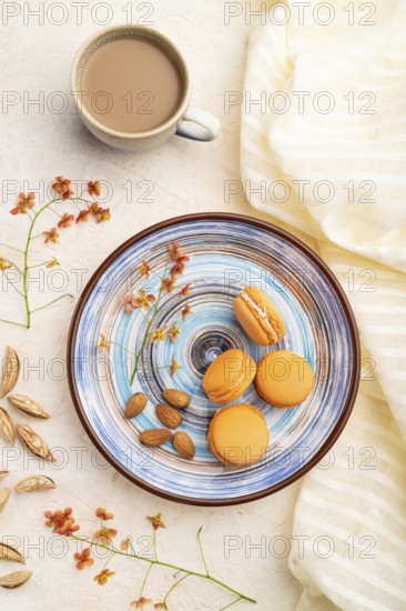 Orange macarons or macaroons cakes with cup of coffee on a white concrete background and linen