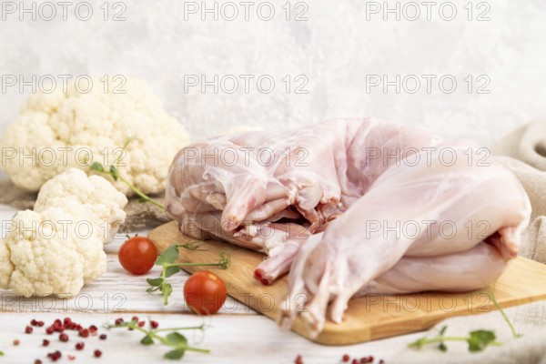 Whole raw rabbit with cauliflower, tomatoes and spices on a white wooden background and linen