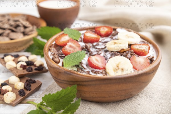 Chocolate cornflakes with milk and strawberry in wooden bowl on white wooden background and linen