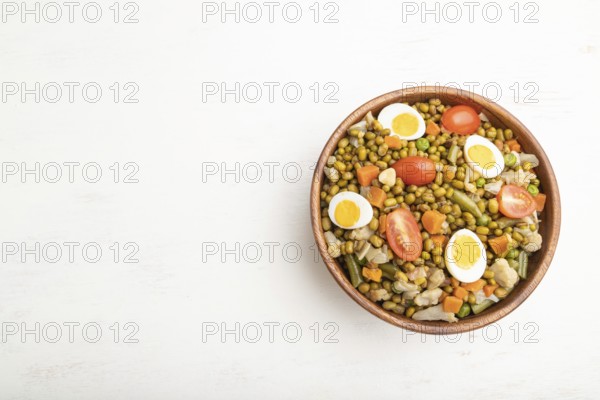 Mung bean porridge with quail eggs, tomatoes and microgreen sprouts on a white wooden background.