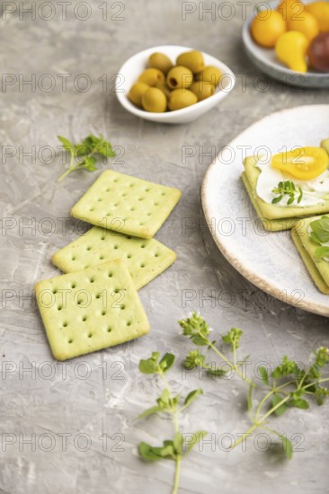 Green cracker sandwiches with cream cheese and cherry tomatoes on gray concrete background. side