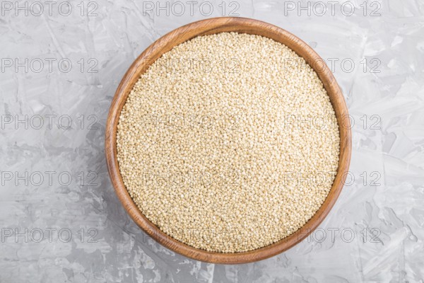 Wooden bowl with raw white quinoa seeds on a gray concrete background. Top view, flat lay, close up