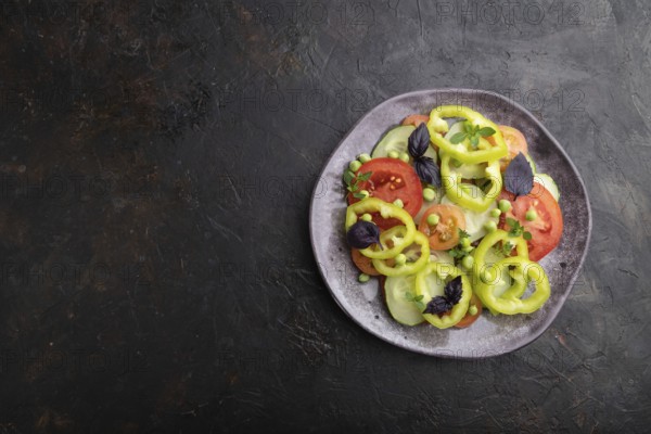 Vegetarian salad from green pea, tomatoes, pepper and basil on a black concrete background. top