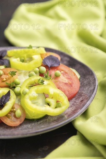 Vegetarian salad from green pea, tomatoes, pepper and basil on a black concrete background and