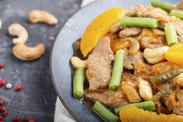 Fried pork with peaches, cashew and green beans on a black concrete background. Top view, close up,