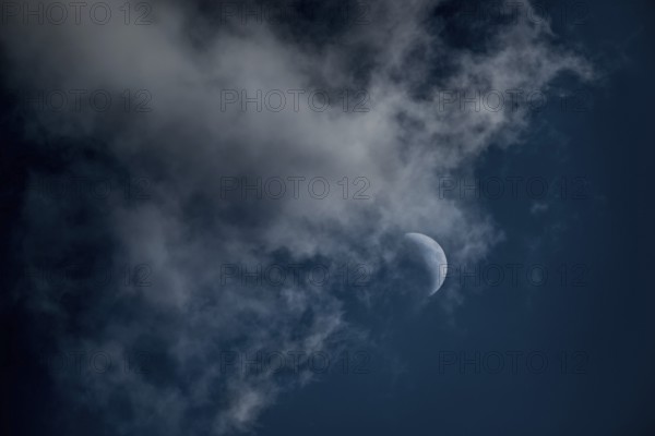 The crescent of the waxing moon in the second quarter shines in a cloudy, dark blue sky,
