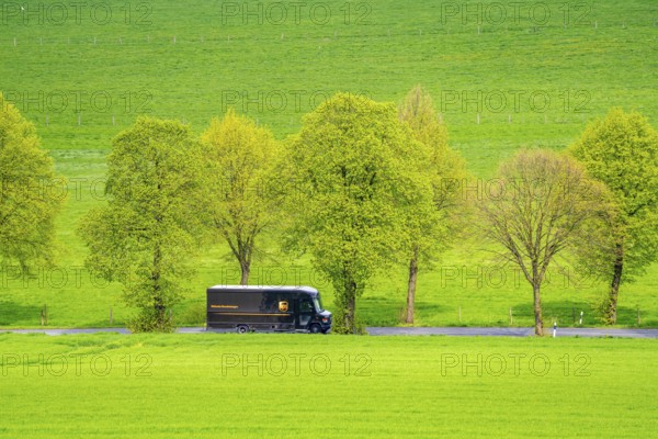 UPS delivery van on a country road, green fields, meadows, trees line the 2-lane road, spring, near