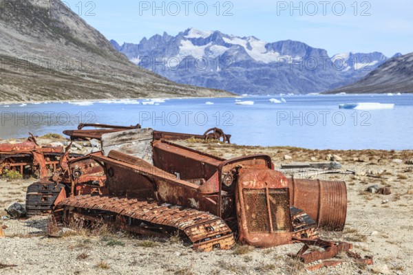 Rusty cars and barrels on a fjord in front of steep mountains, remains of a US airbase from the